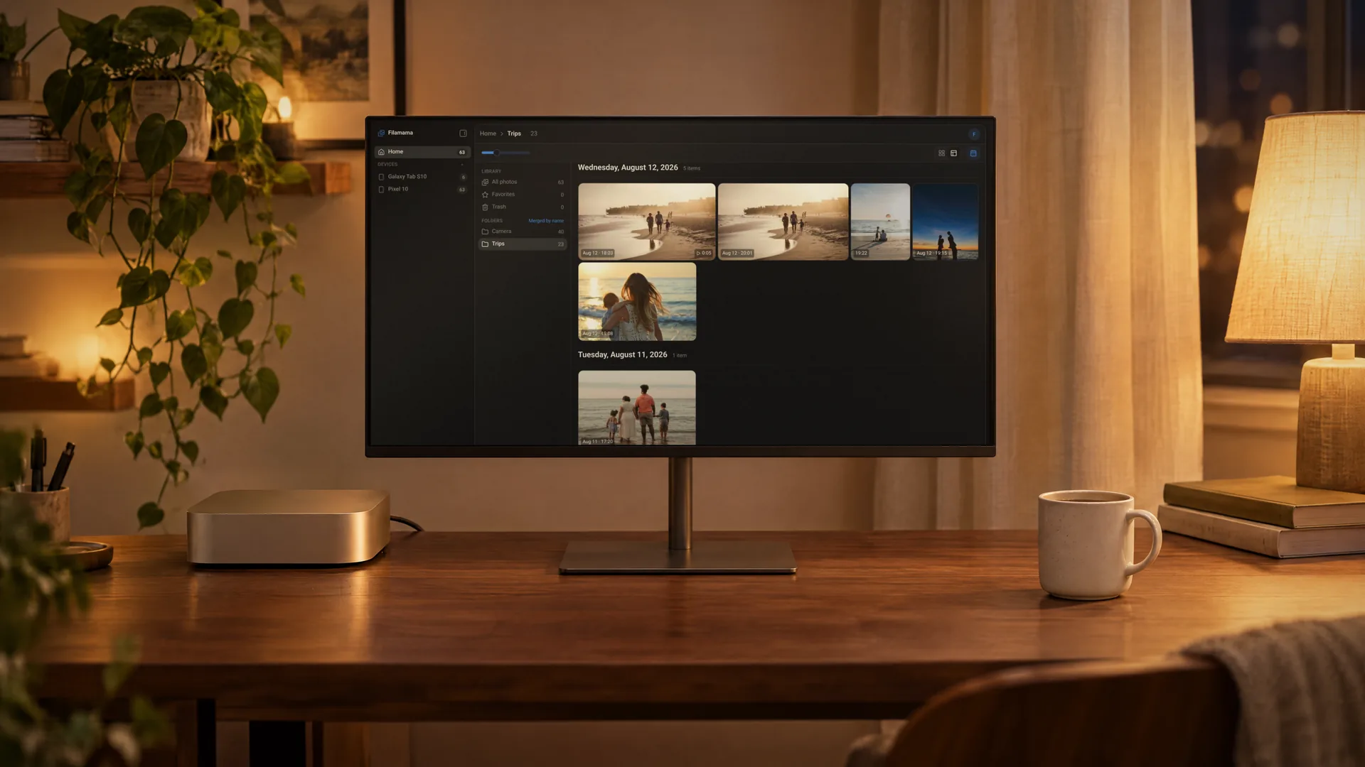 A silver Mac mini next to a monitor on a walnut desk at night, the monitor showing the Filamama Trips folder in mosaic view