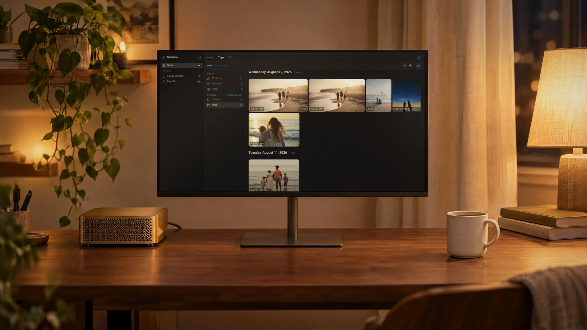 A small desktop computer next to a monitor on a walnut desk at night, the monitor showing the Filamama Trips folder in mosaic view